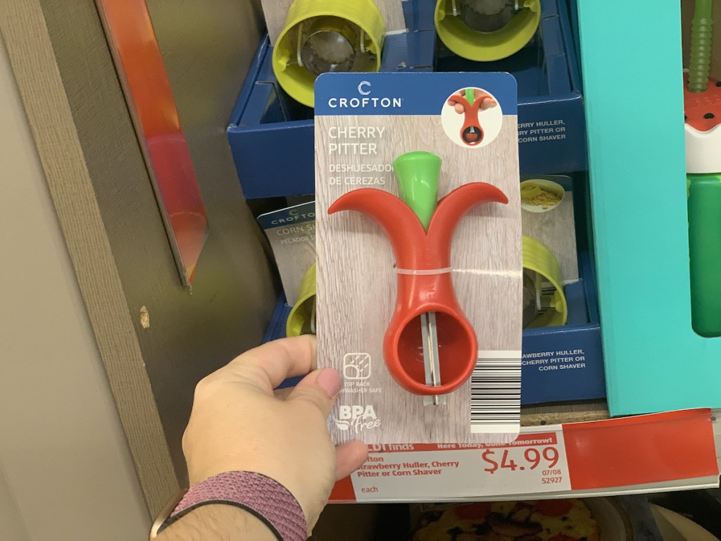 hand holding crofton cherry pitter at aldi with corn shucker behind