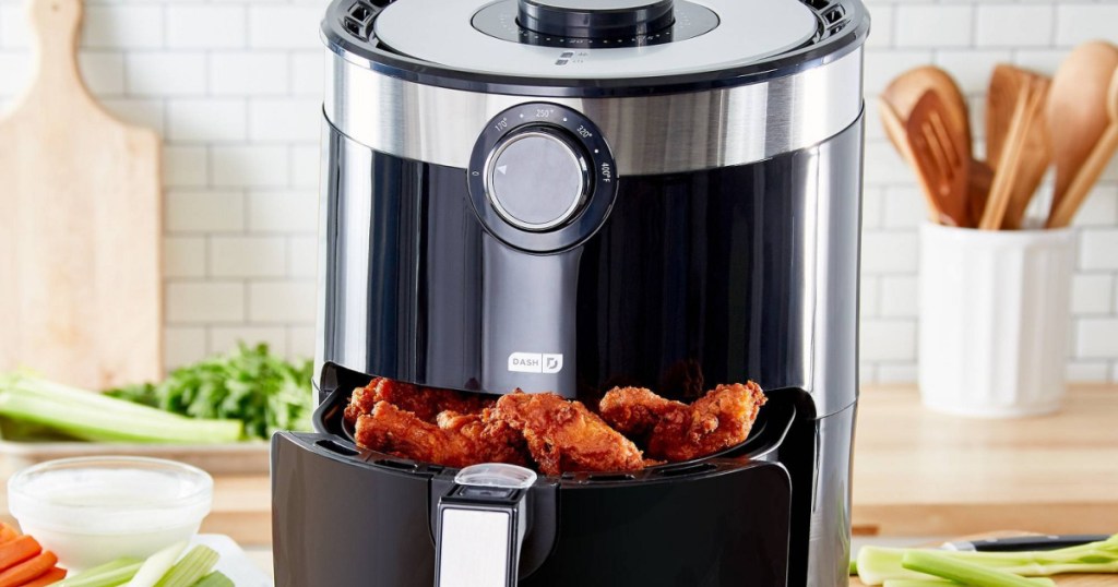 black air fryer filled with chicken wings on kitchen counter with plates of celery and veggies