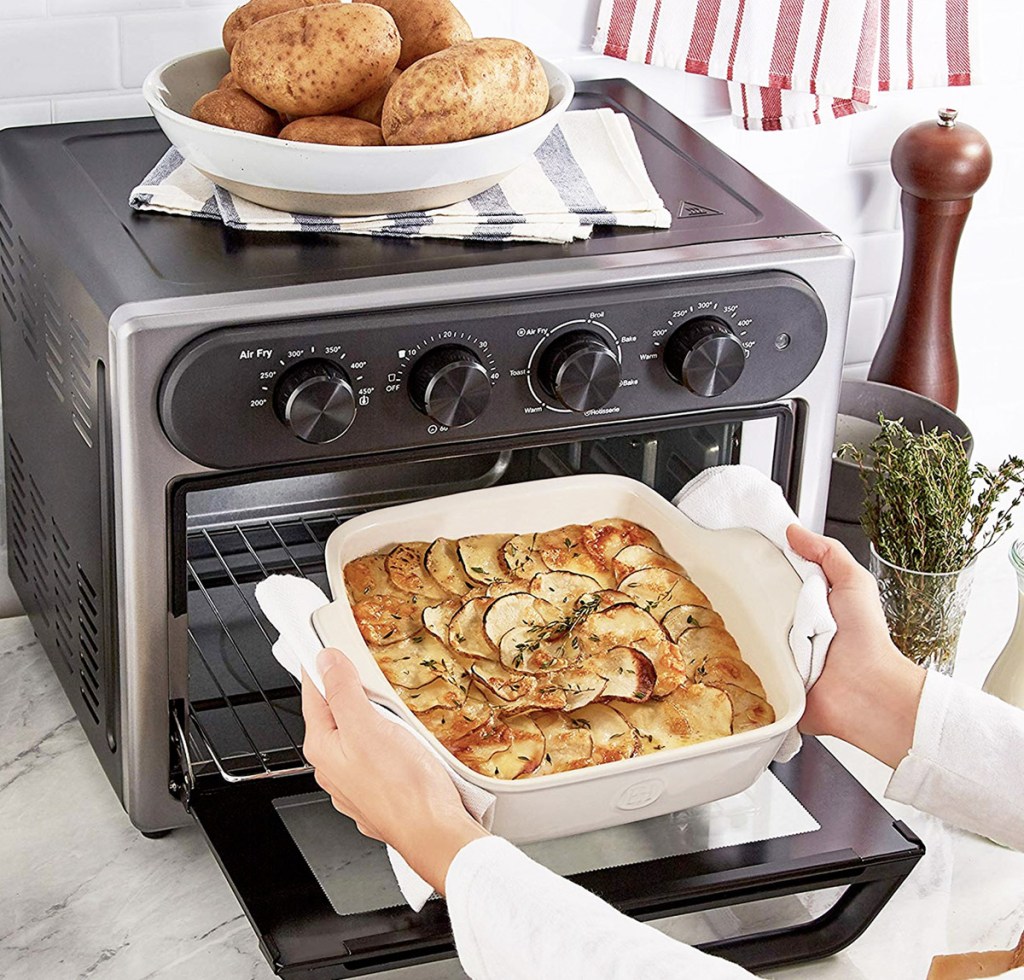 stainless steel and black convection toaster oven open on kitchen counter with person taking out casserole