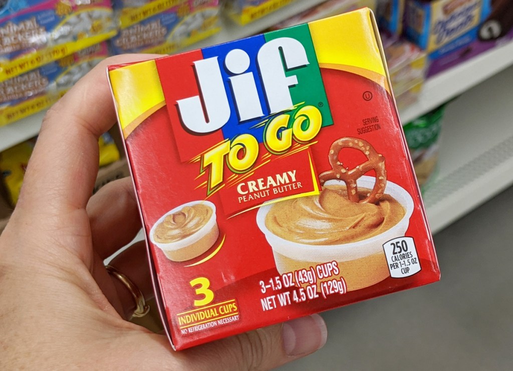 person holding up a red box of jif to-go creamy peanut butter