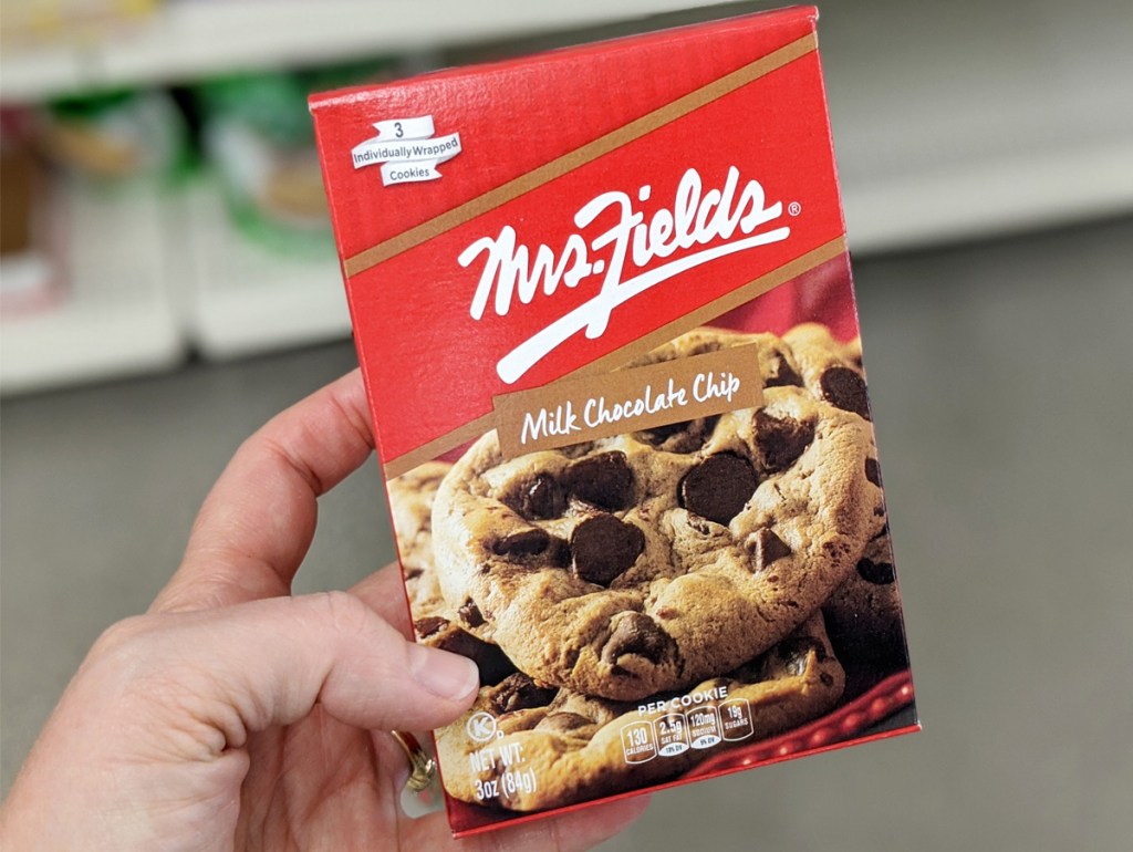 person holding up a red box of individually wrapped mrs fields chocolate chip cookies