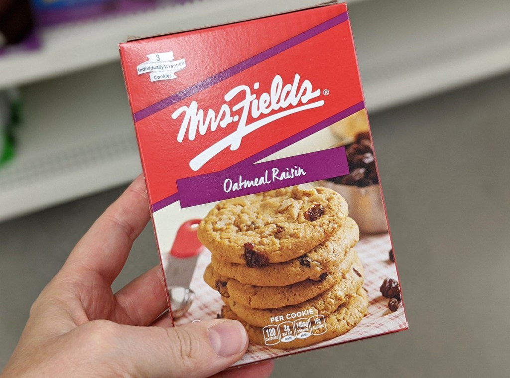 person holding up a red box of individually wrapped mrs fields oatmeal raisin cookies