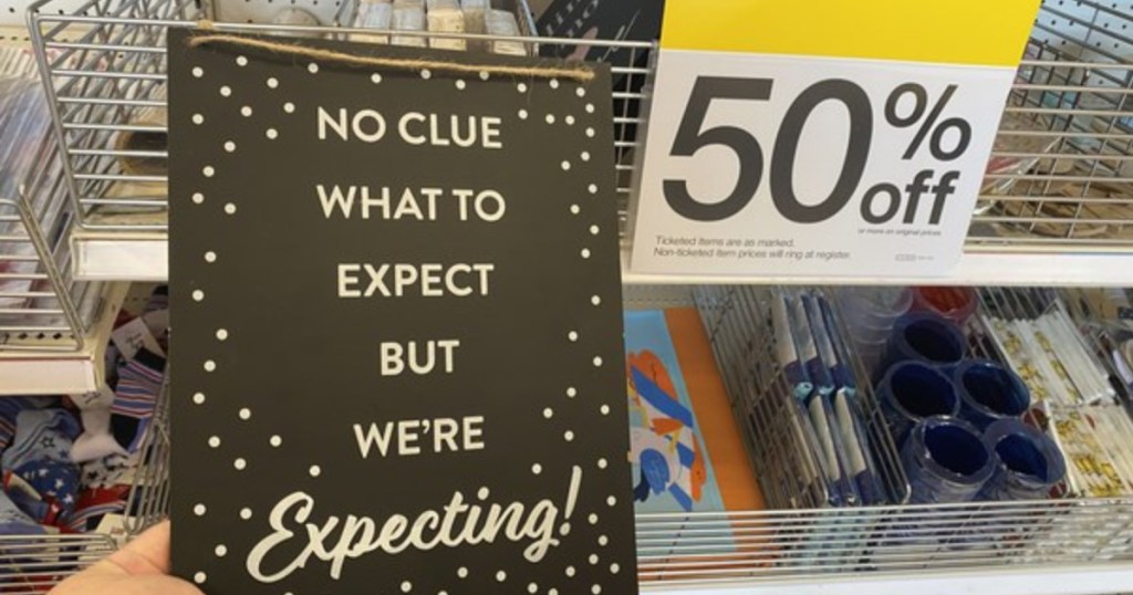 hand holding sign that says no clue what to expect but we are expecting next to clearance 50% off sign at target
