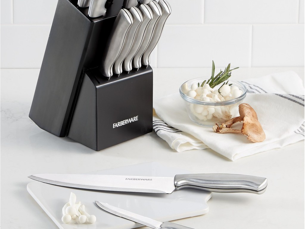 black knife block with stainless steel cutlery on counter with two knives on plate and bowl of garlic