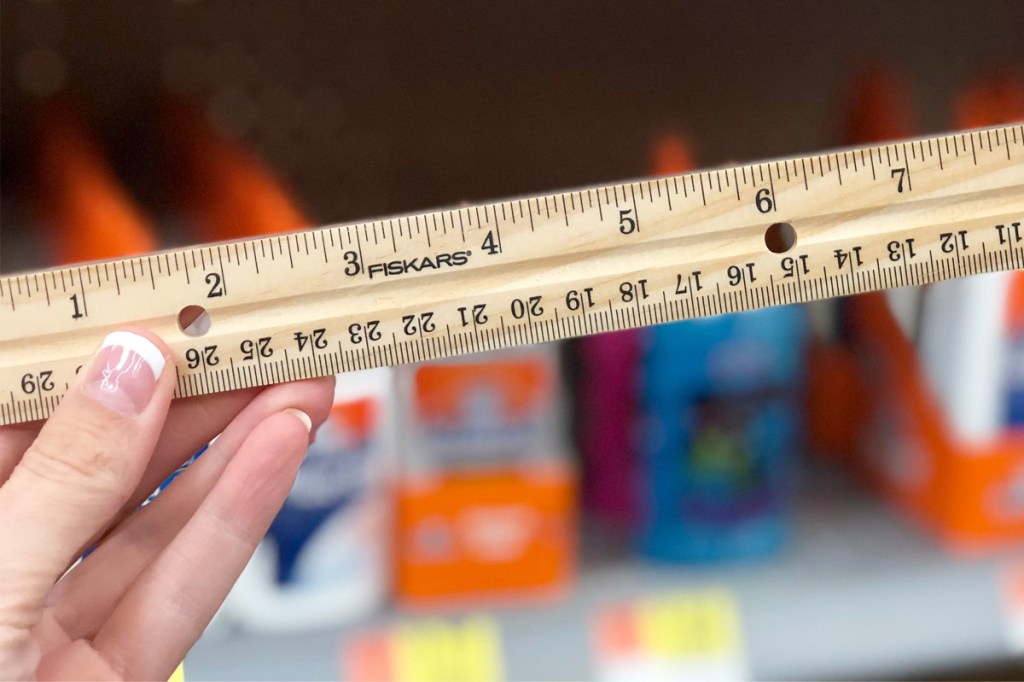 person holding up wooden fiskers brand ruler in front of store shelves of school supplies