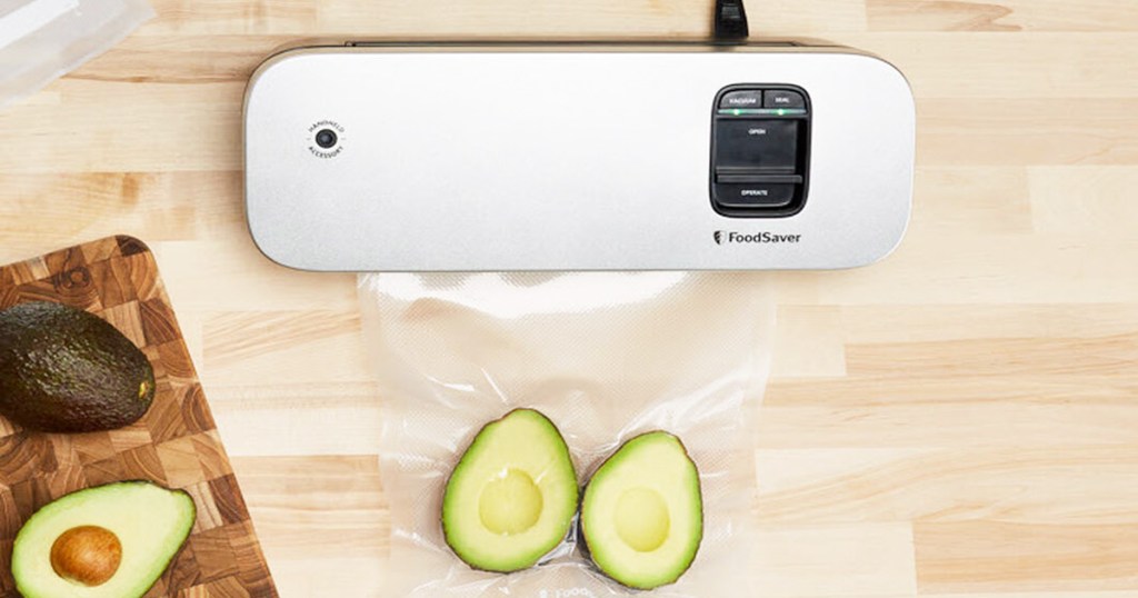 silver foodsaver vacuum on wood countertop sealing plastic bag around avocado halves