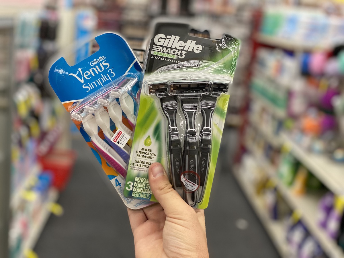 man hand holding a pack of each Gillette venus simply 3 and mach 3 disposable razors in cvs