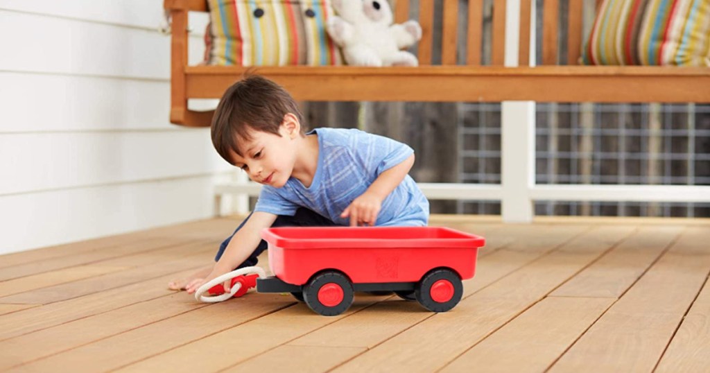 little boy playing with red wagon on deck