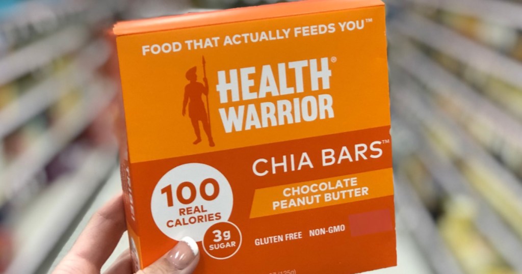 manicured hand holding box of chocolate peanut butter chia bars in store aisle