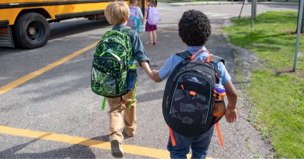 two kids wearing backpacks getting on a school bus