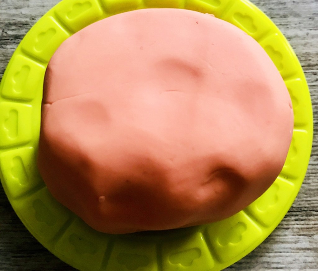 ball of red homemade play-dough sitting on small plastic green plate