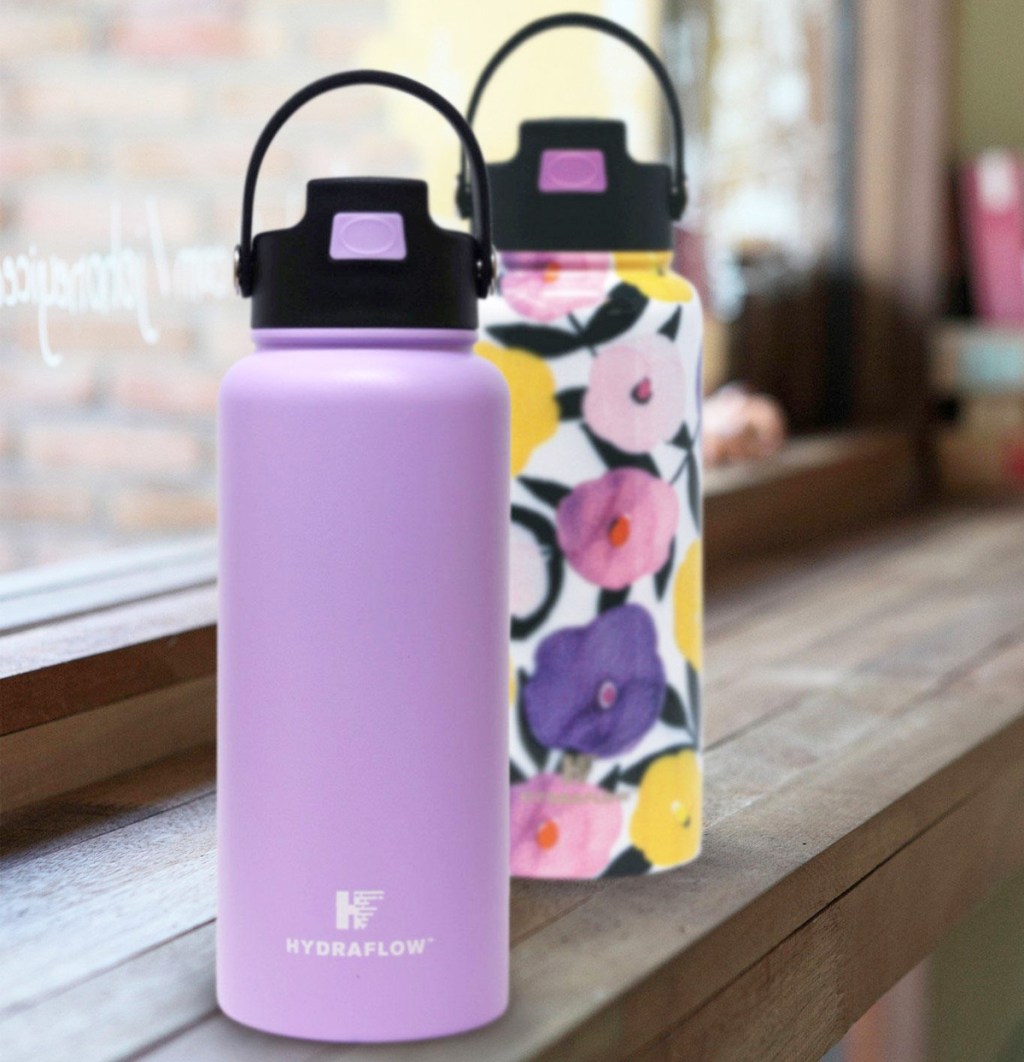 two stainless steel water bottles on wood windowsill in purple and floral print colors