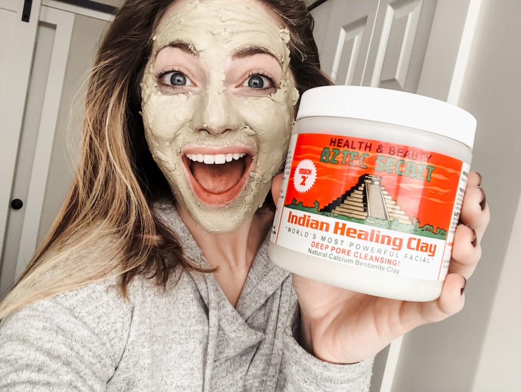 woman holding Indian healing clay canister beauty product with green mask on face