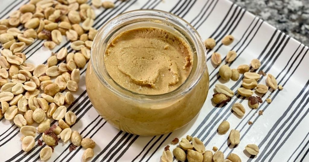 A jar of peanut butter next to some peanuts 
