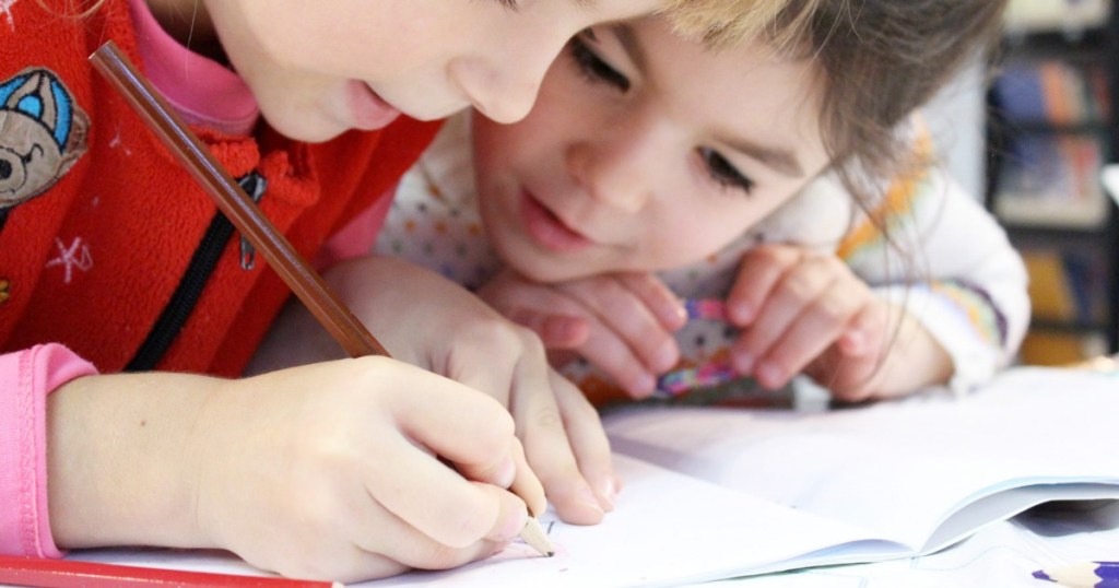 two young kids using colored pencils to draw in workbook
