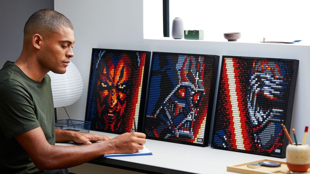 man sitting at desk writing with LEGO art pieces next to him