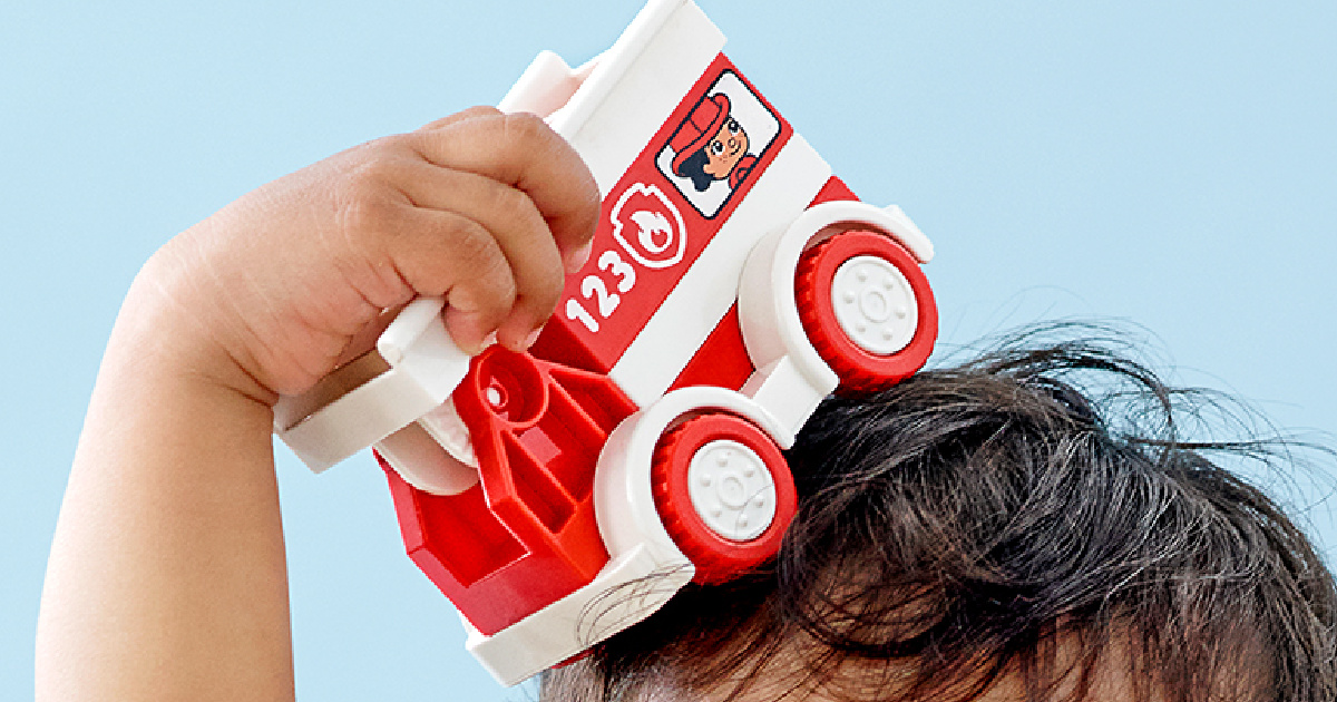 small child holding a lego duplo red fire truck on top of his head
