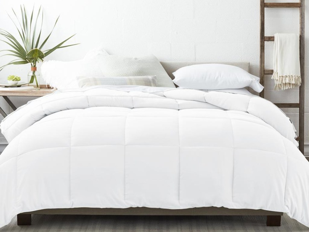 white down alternative comfofter set on a bed with pillows next to a wooden shelf
