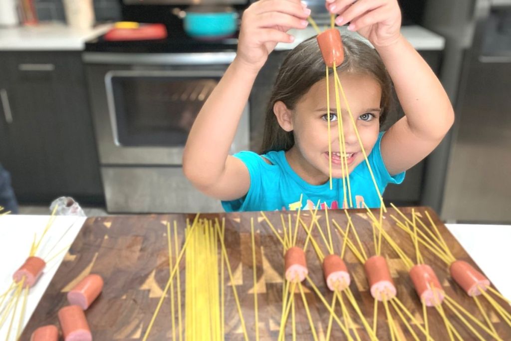 A little girl making threading noodles into hot dog pieces