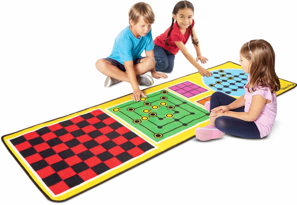three kids on floor with large rug printed with different game boards