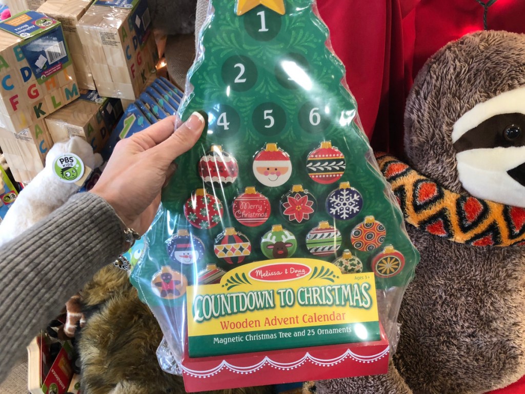 hand holding christmas tree advent calendar with stuffed animals and toys behind