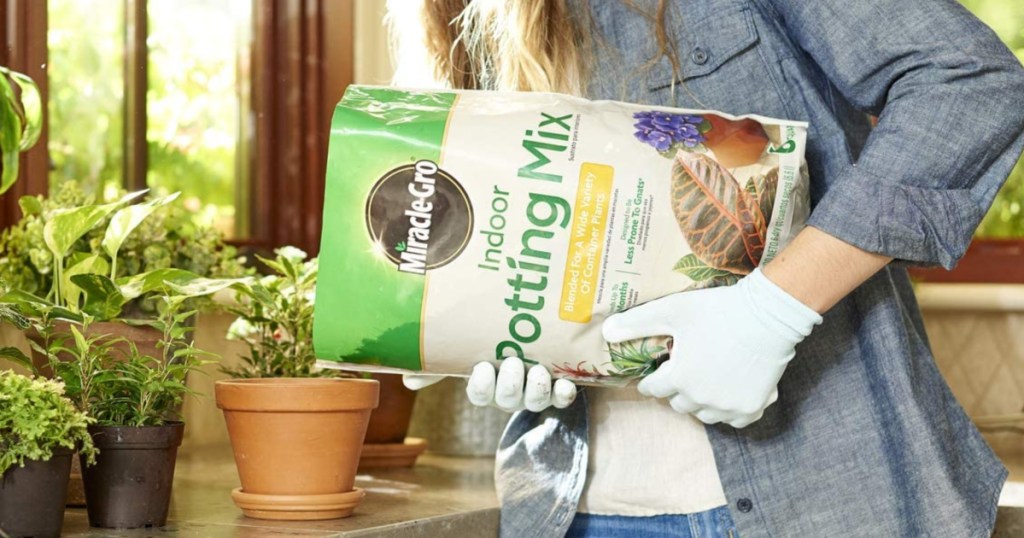 woman wearing white gloves pouring miracle gro potting soil into a planter