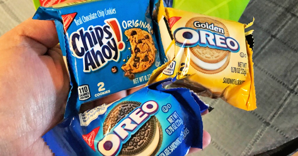 hand holding three individual packages of oreo, chips ahoy, and golden oreo cookies