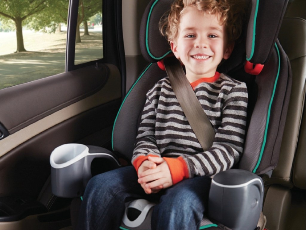 boy sitting in black and teal car seat booster