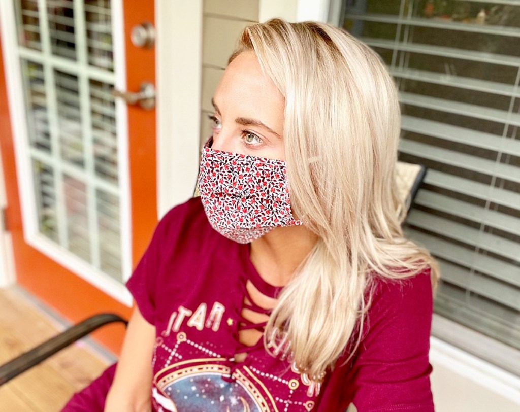 woman with blonde hair sitting outside house wearing red graphic tee and floral print face mask