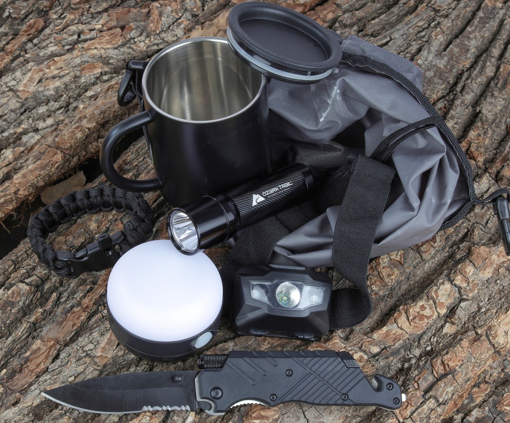 camping tool set with lights, headlamp, coffee mug, and waterproof bag placed on a tree stump