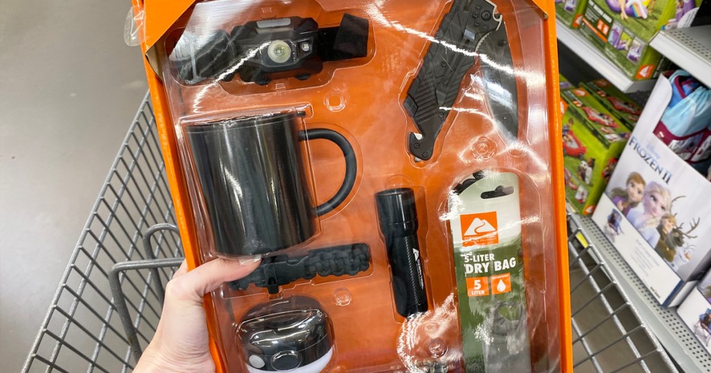 person holding up an orange box of camping tools with coffee mug, lights, and multi-tool