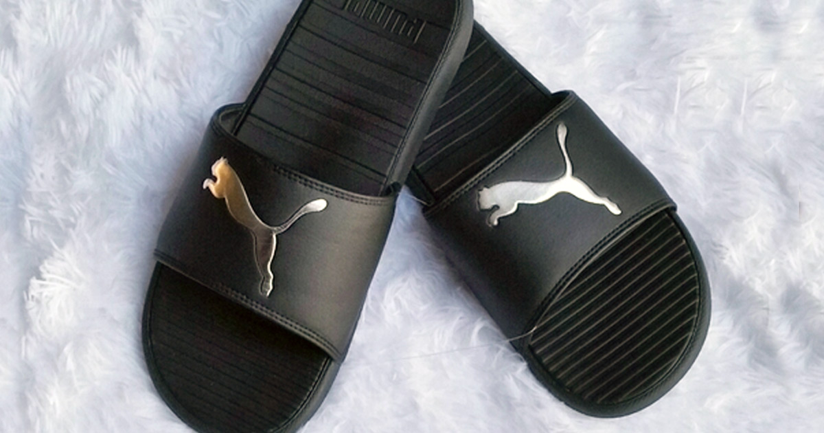 pair of black puma slides with cat logo on top on a white fluffy blanket