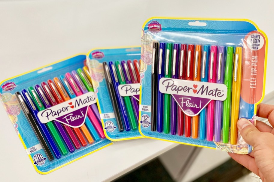 person holding package of multi colored papermate pens with two more packages in background