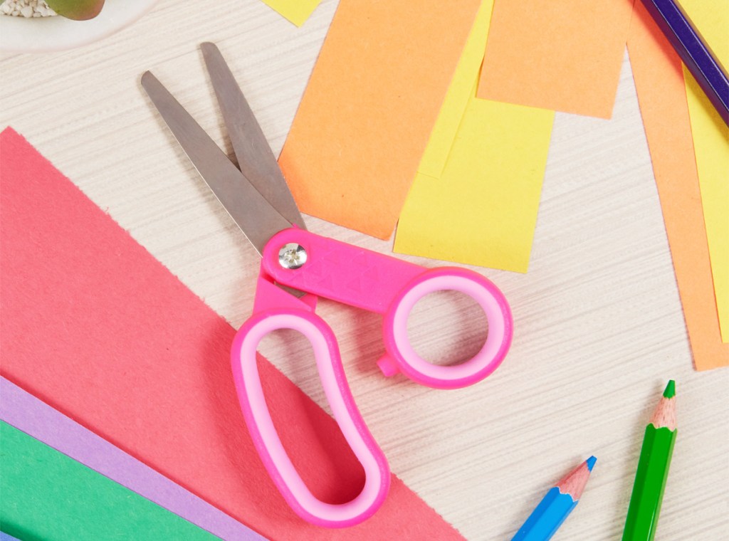 pair of pink kids scissors laying on top of cut pieces of construction paper