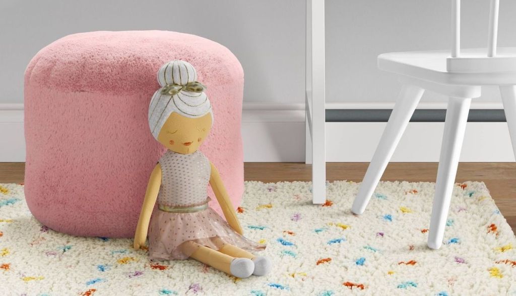 doll leaning against pink pouf ottoman