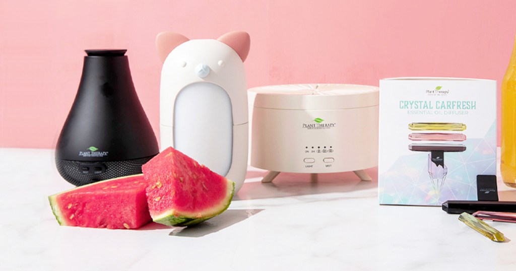 various different oil diffusers sitting on white marble table with watermelon slices and pink background