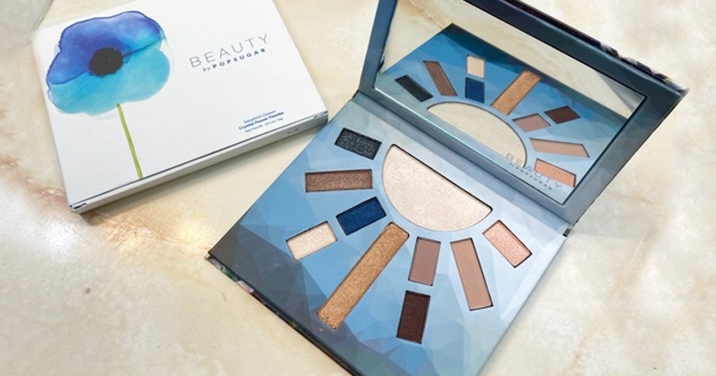 blue themed eyeshadow pallete open on marble counter next to the white box with blue flower it comes packaged in