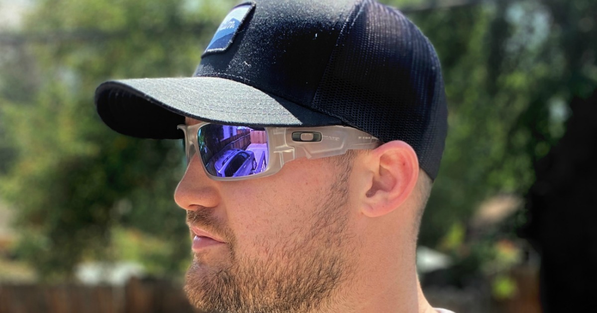 Man wearing name brand sun glasses with blue lenses and a black baseball cap