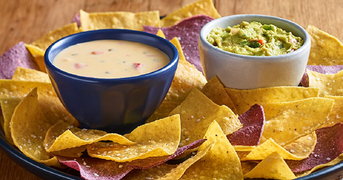 plate of tortilla chips on table with small bowls of queso and guacamole