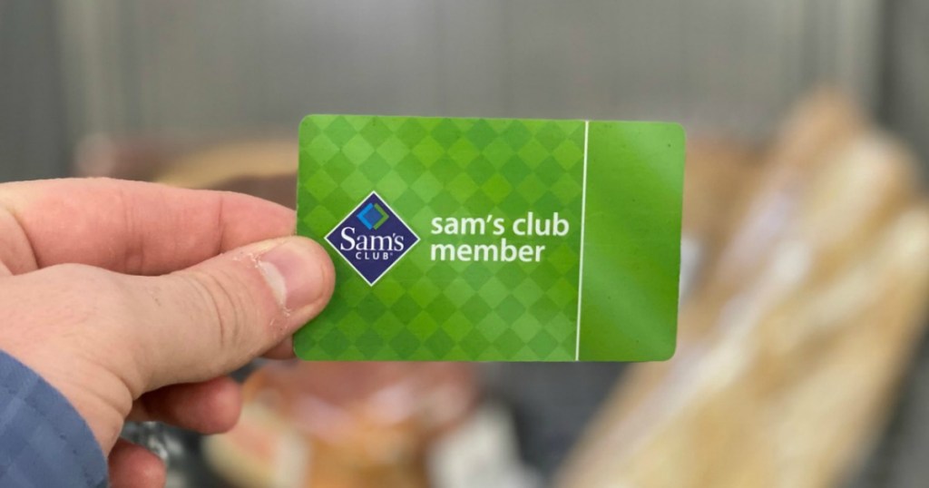 Man's hand holding a green Sam's Club Membership card near a shopping cart