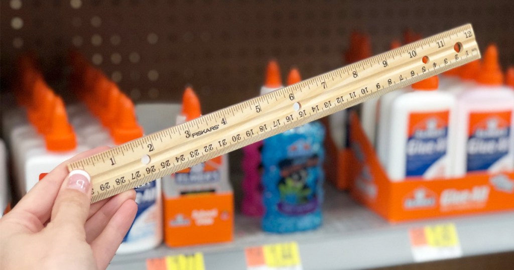 person holding up wooden fiskers brand ruler in front of store shelves of school supplies