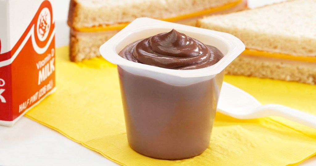 individual chocolate pudding cup on yellow napkin with carton of milk and cheese sandwich in background