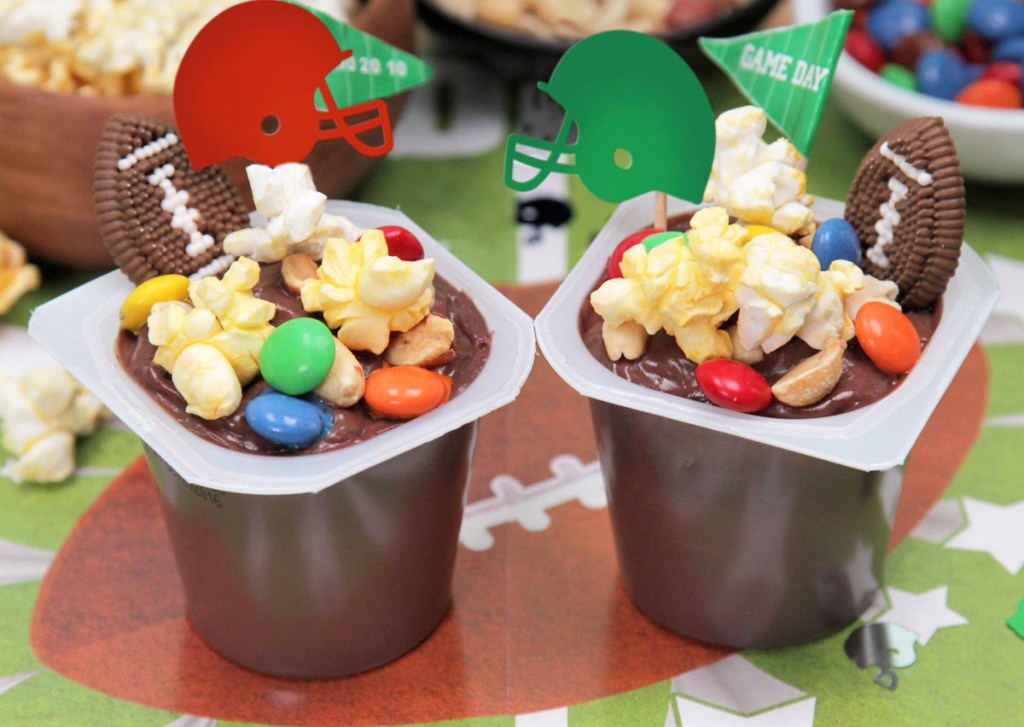 chocolate pudding cups with m&ms, popcorn, and football helmets on football themed tablecloth