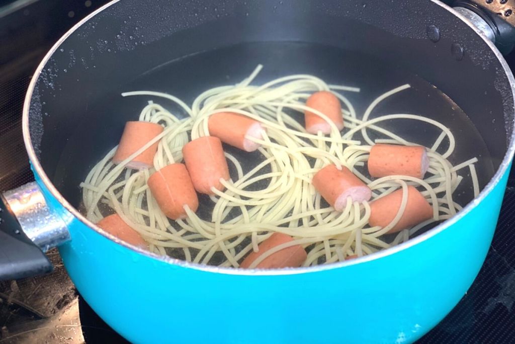 Noodles and hot dogs boiling in a pot of water on the stove