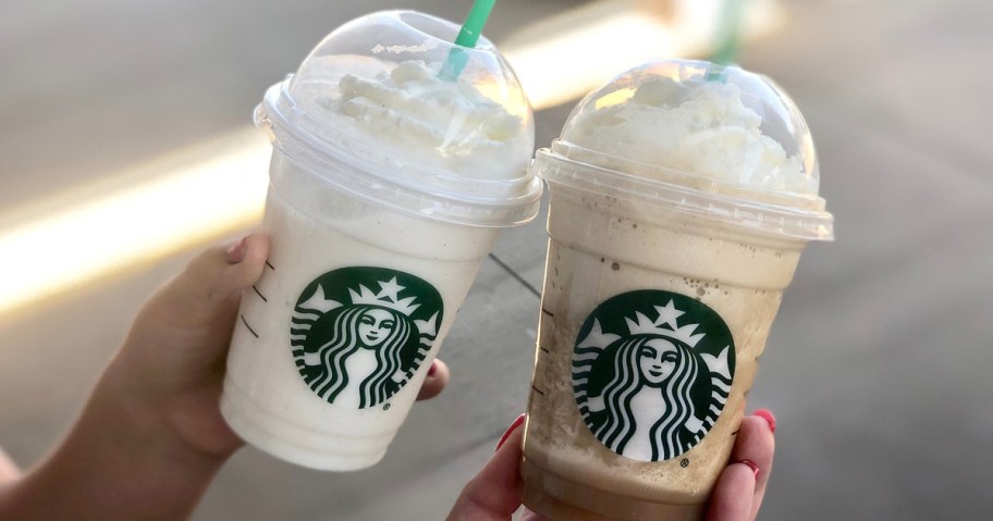two people holding up starbucks frappuccinos with whipped cream and green straws