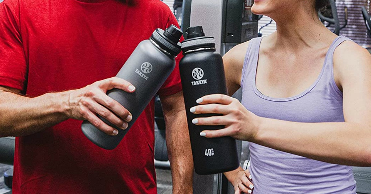 Two adults in a gym holding large stainless steel water bottles