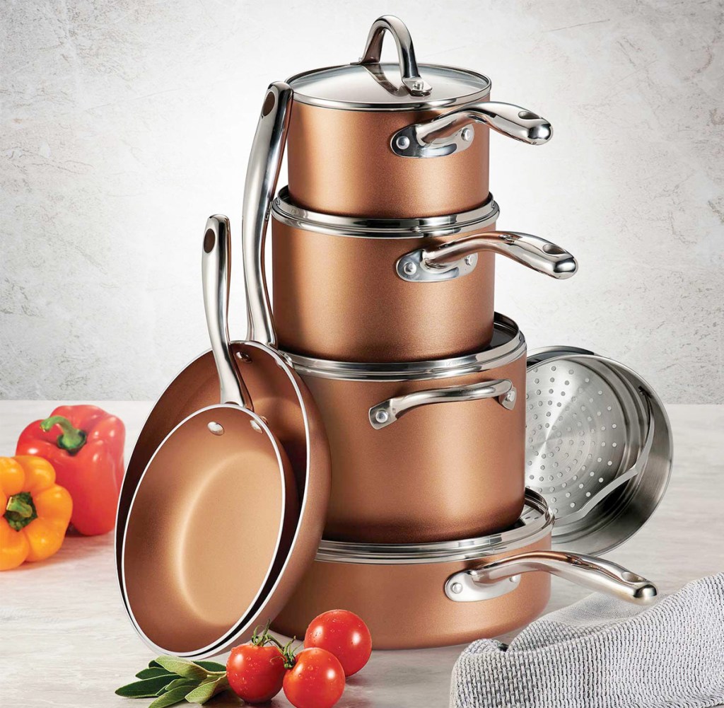 copper colored pots and pans stacked on one another with bell peppers and tomatoes near them on counter top