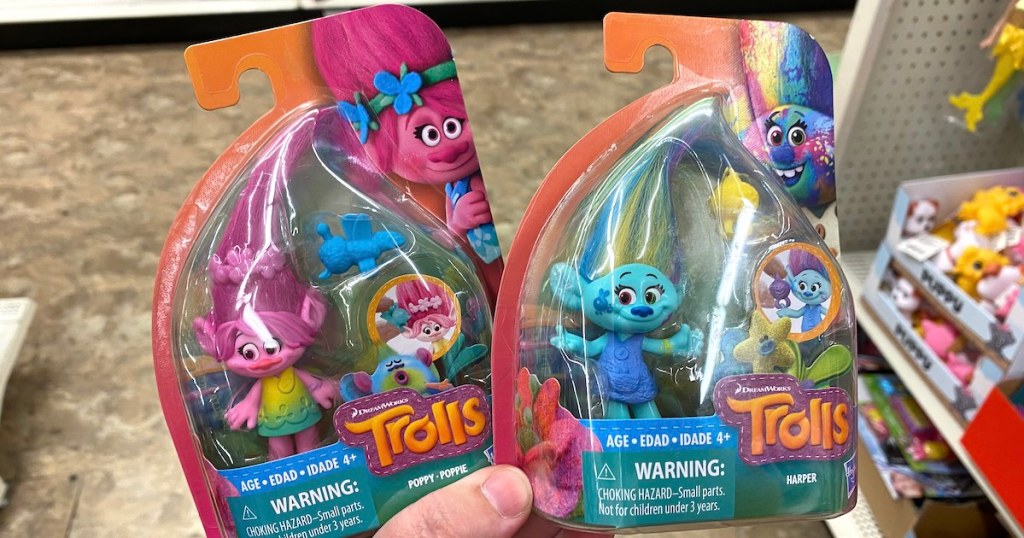 hand holding two packs of trolls action figures in dollar tree