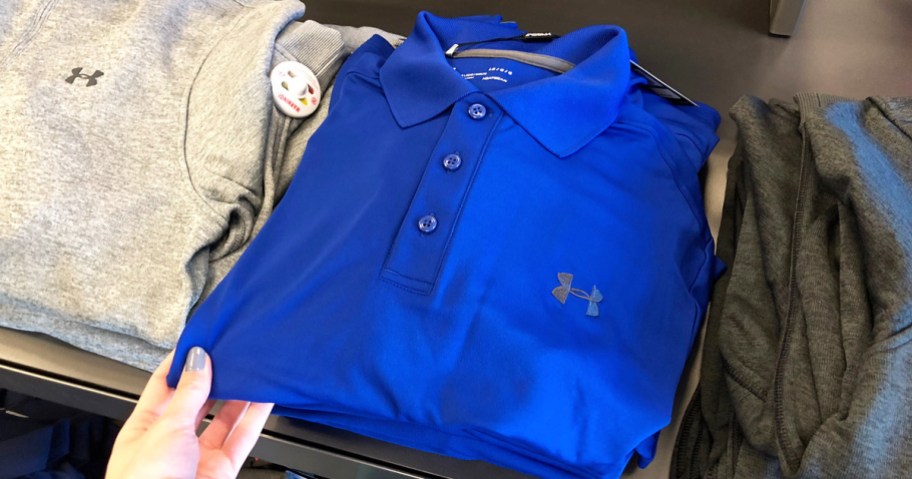 person holding a folded blue under armoud brand polo on a store display table