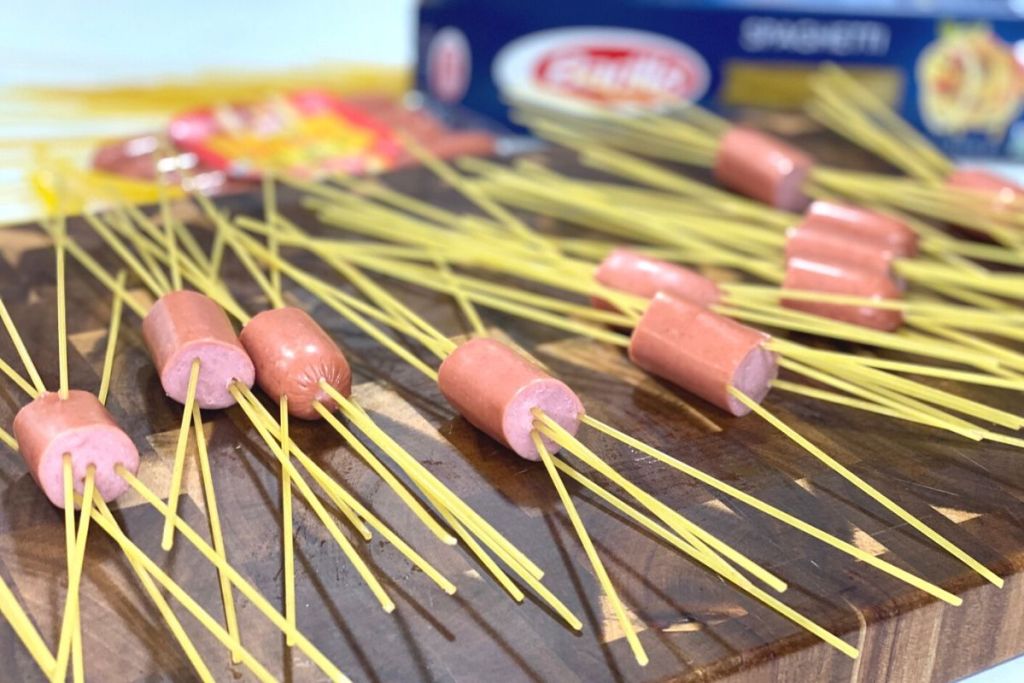 Hot dogs with noodles thredded through them on a cutting board